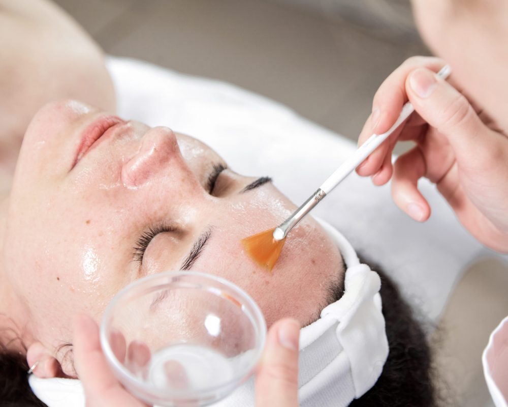 Facial peeling, skin treatment. A dermatologist applies of phytic acid with a white fan brush on female face. A caucasian woman in cosmetic clinic. Cosmetology, facial skin care. Girl in beauty salon